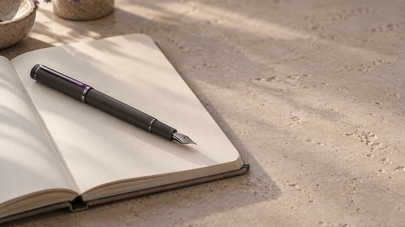 A pen resting on an open notebook on a quiet stone desk in morning light.
